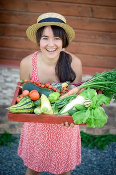 happy young girl holding harvest of vegetables next to wooden background. High quality photo