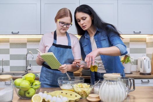 Mother and teenage daughter cooking at home in kitchen. Mom and girl making apple pie together, talking, use recipe book. Relationships, communication parent teenager, healthy homemade food, family