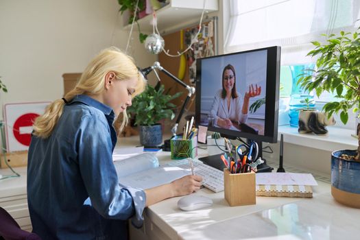 Teenage girl studying at home online using a computer. Virtual lesson, female teacher on the screen talking to a student, teaching remotely. E-learning, video conference, adolescence, high school concept