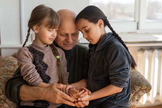 grandfather and two granddaughters hugging on sofa at home.