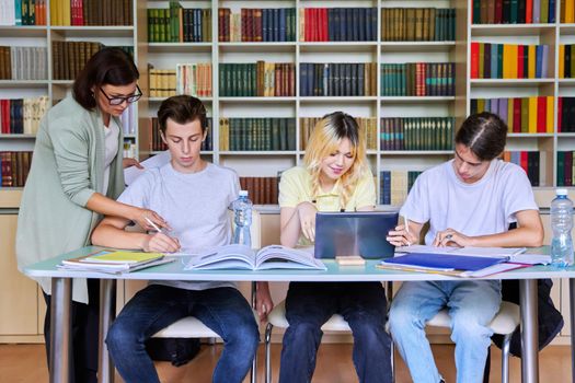 Group of teenage students studying in library class with female teacher. Mentor helping schoolchildren sitting at desks. High school, education, adolescent, back to school, back to college concept