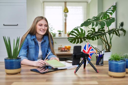 Online English lesson, young woman teaching English to students, using smartphone on tripod. Virtual lesson, teacher teaching remotely, recording video lesson.