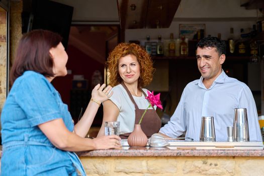 Couple working at the bar in an outdoor cafe talking to a female client, hotel restaurant family small business, business owners, workplace, staff concept