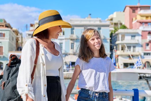 Mom and preteen daughter walking talking together. Embankment of sea city, summer sunny landscape of bay with yachts, tourist destination, communication parent and teen child, family vacation concept