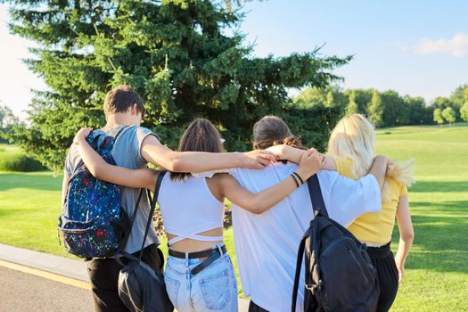 Happy teenage friends hugging together on sunny day in park. Group of teenagers together, back view. Friendship, adolescence, summer, vacation, lifestyle, fun, happiness, holiday, leisure people
