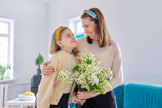 Happy mother and daughter child congratulating with bouquet of flowers and hand-drawn card, at home in living room. Mother's day, family, relationship, emotions, love, togetherness concept