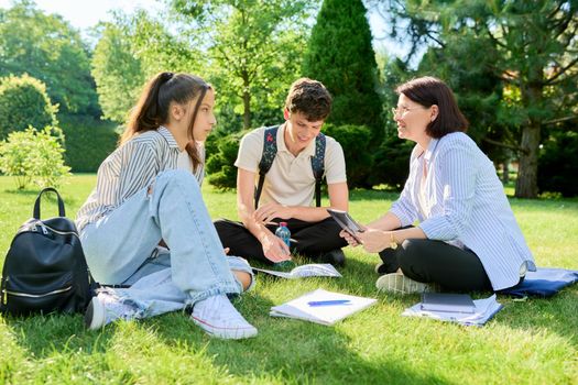 School teacher, psychologist, social worker talking to teenagers. Woman with teenage schoolchildren sitting on grass on campus lawn. Education, high school, psychology, mental health, adolescence