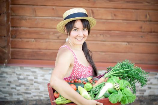 happy young girl holding harvest of vegetables next to wooden background. High quality photo