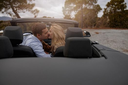 Happy man and woman sitting in convertible car outdoor and kissing, travel together, love concept