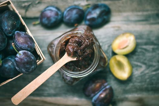 plum jam in glass jar with spoon on wooden background. High quality photo