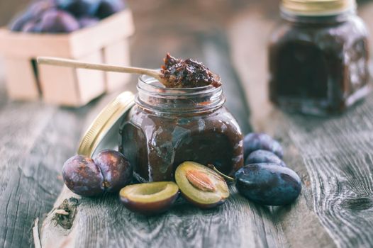 plum jam in glass jar with spoon on wooden background. High quality photo