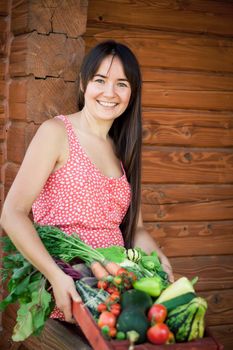 happy young girl holding harvest of vegetables next to wooden background. High quality photo