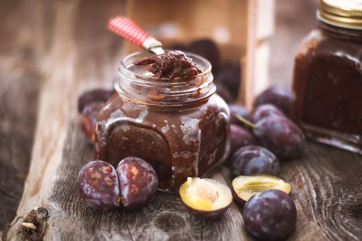 plum jam in glass jar with spoon on wooden background. High quality photo