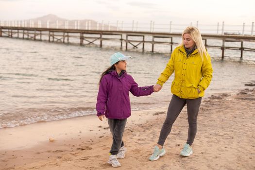 Portrait of mother with her daughter playing near the cold sea.