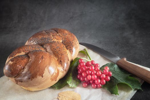 A loaf of white bread with a crisp crust, sprinkled with poppy seeds, and viburnum berries on the table. Front view, where you want to copy.