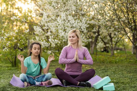 Young woman with little daughter in a sporty uniform doing yoga of a house by the garden.