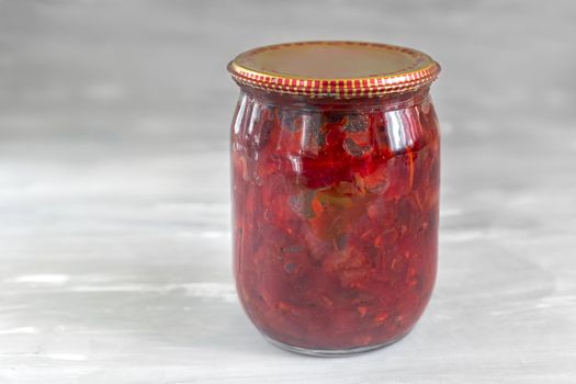 Home preservation: in a glass jar, beets, canned with tomatoes, onions, carrots for cooking borscht, closed with a metal lid. Front view, copy space
