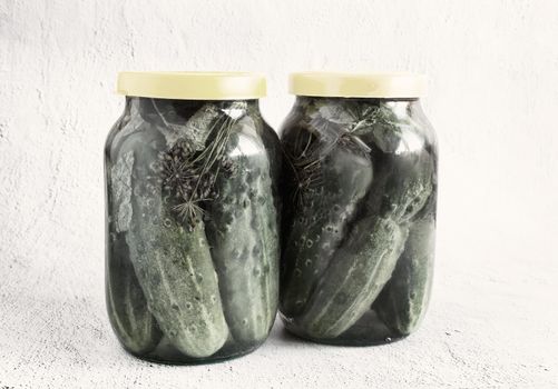 Two glass jars with pickled cucumbers, covered with lids. The concept of preserving organic products. Front view, copy space.