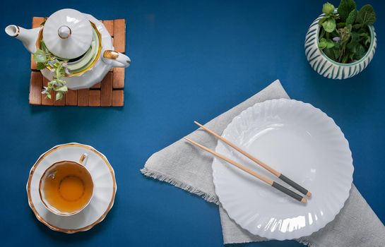 On the table is an empty plate, chopsticks, a teapot, and a Cup of herbal tea. The pattern of Japanese cuisine. Top view with space to copy. Flat lay