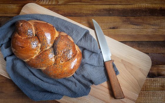 A loaf of white bread with a crisp crust, sprinkled with poppy seeds and a knife on the kitchen Board. Top view, copy space.