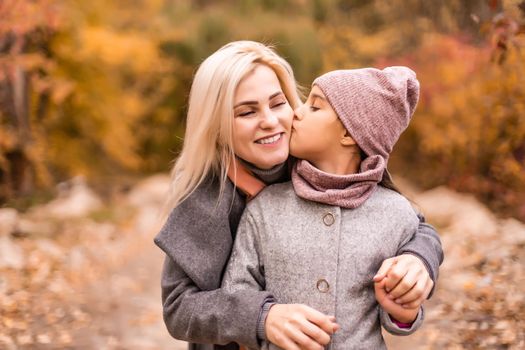 Mother and daughter having fun in the autumn park among the falling leaves