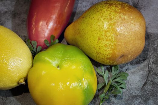 On the table on a napkin are ripe fruits: lemon, tangerine, pear and bulgarian red pepper. Top view, close-up.