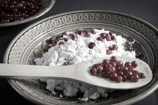 On the table in a ceramic plate delicious natural cottage cheese with red currant berries. Close-up, front view