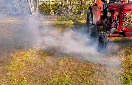 red exhaust tractor, heavy agricultural machine releasing emission pollution gas into the air,