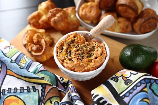 ricotta dip with sun-dried tomatoes and baked paprika in a ceramic white bowl and homemade popovers, which is a puffed, airy, and eggy hollow roll, is fresh from the oven.