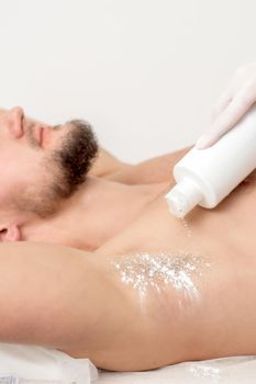 Hand of master depilation pouring talcum powder on armpit of young man before depilation procedure.