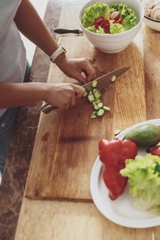 Chopping vegetables with a knife on a wooden kitchen board. Two bowls with vegetables and herbs