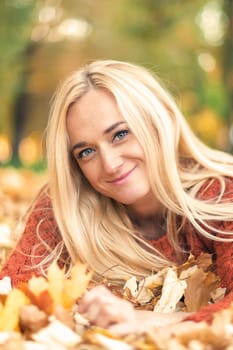 Beautiful young blond hair caucasian woman lies down on leaves at the autumn park