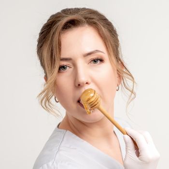 Portrait of beautiful young caucasian woman eating honey with wooden spoon on white background