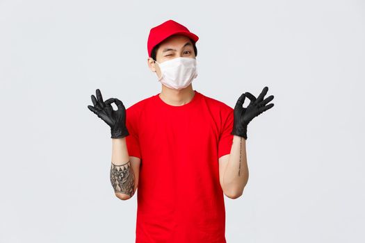 Keep calm and rely on our deliver company. Cheerful relaxed asian delivery guy in red cap and t-shirt, show zen, nirvana gesture and wink, assure your package safe. Courier stay peaceful.