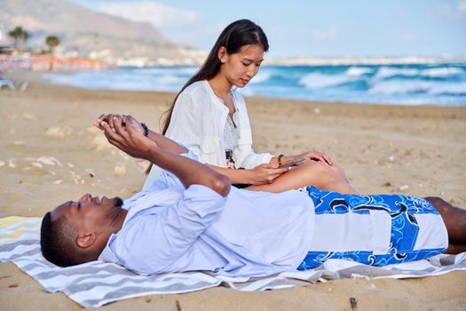 Young couple relaxing on the beach, lying sitting on the sand with smartphones. Summer autumn vacation together, lifestyle. technology, family concept