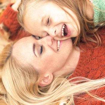 Little girl and young caucasian mom lying down directly above looking at camera on autumn leaves