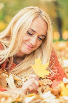 Beautiful young blond hair caucasian woman lies down on leaves at the autumn park