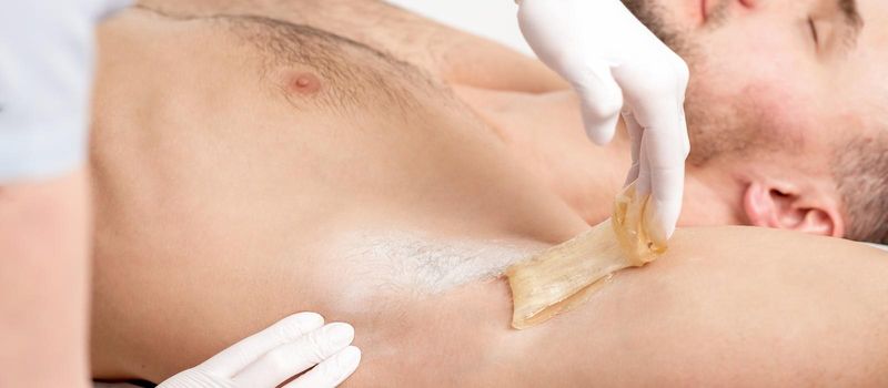 Depilation and epilation male armpit with liquid sugar paste. Hand of cosmetologist applying wax paste on armpit of man. Smooth underarm concept