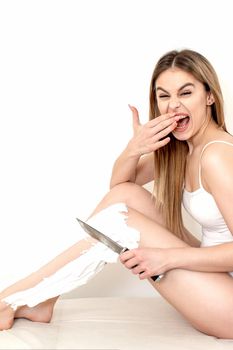 Beautiful young caucasian woman shaves her legs with a knife on a white background