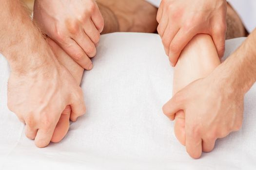 Hands of two massagers giving massage to soft bare feet during spa foot treatment. Massage in four hands.
