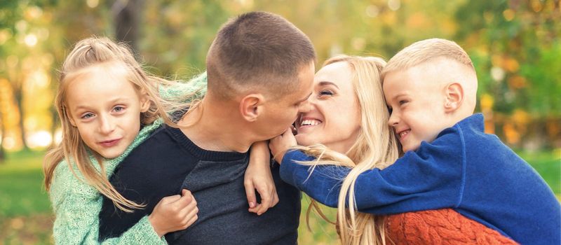 Portrait of young family playing in autumn park. Parents kissing and resting with children in the autumn park