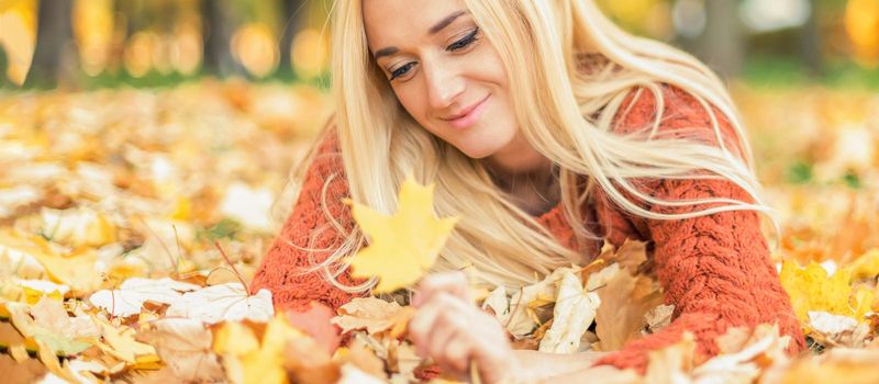 Beautiful young blond hair caucasian woman lies down on leaves at the autumn park