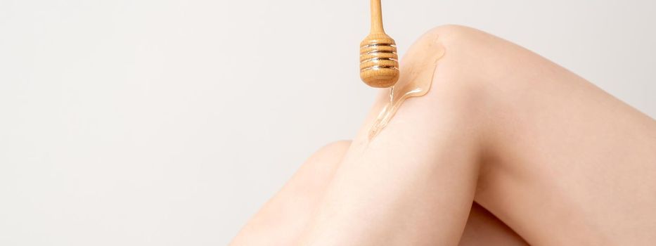 Wax on honey stick flowing down on female leg in human hand wearing protective glove on white background