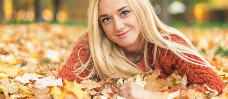 Beautiful young blond hair caucasian woman lies down on leaves at the autumn park