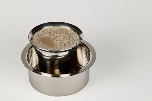 South Indian filter coffee in a steel tumbler and steel dabarah on a white background