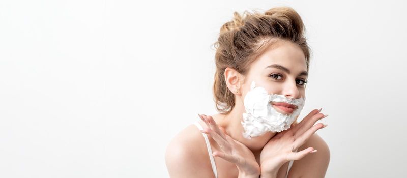 Beautiful young caucasian woman with shaving foam on her face posing on white background