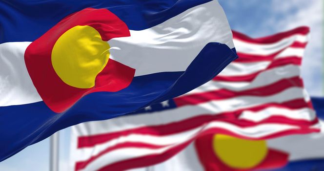 Colorado state flags waving along with the national flag of the United States of America. In the background there is a clear sky.