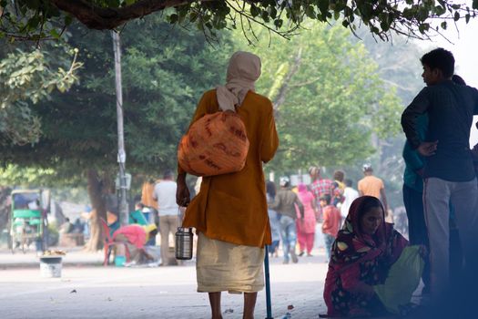 Haridwar, Uttarakhand - circa 2021 : Sadhu monk wearing the saffron robes holy to hinduism and a bag with holy symbols while walking among people on the banks of the sacred river ganga yamuna