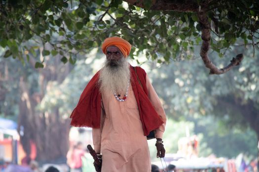 Haridwar, Uttarakhand - circa 2021 : Sadhu monk wearing the saffron robes holy to hinduism and a bag with holy symbols while walking among people on the banks of the sacred river ganga yamuna