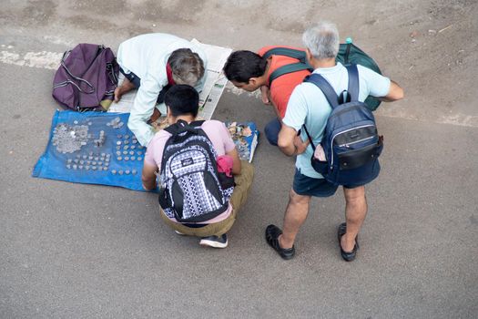 aerial drone shot of a street side coin collector seller with a crowd of people around him looking for collectable old currency from ancient india as a hobby in India